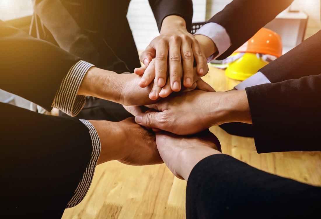 Four employees arms putting their hands into the middle, layering their hands on top of each other to show teamwork.